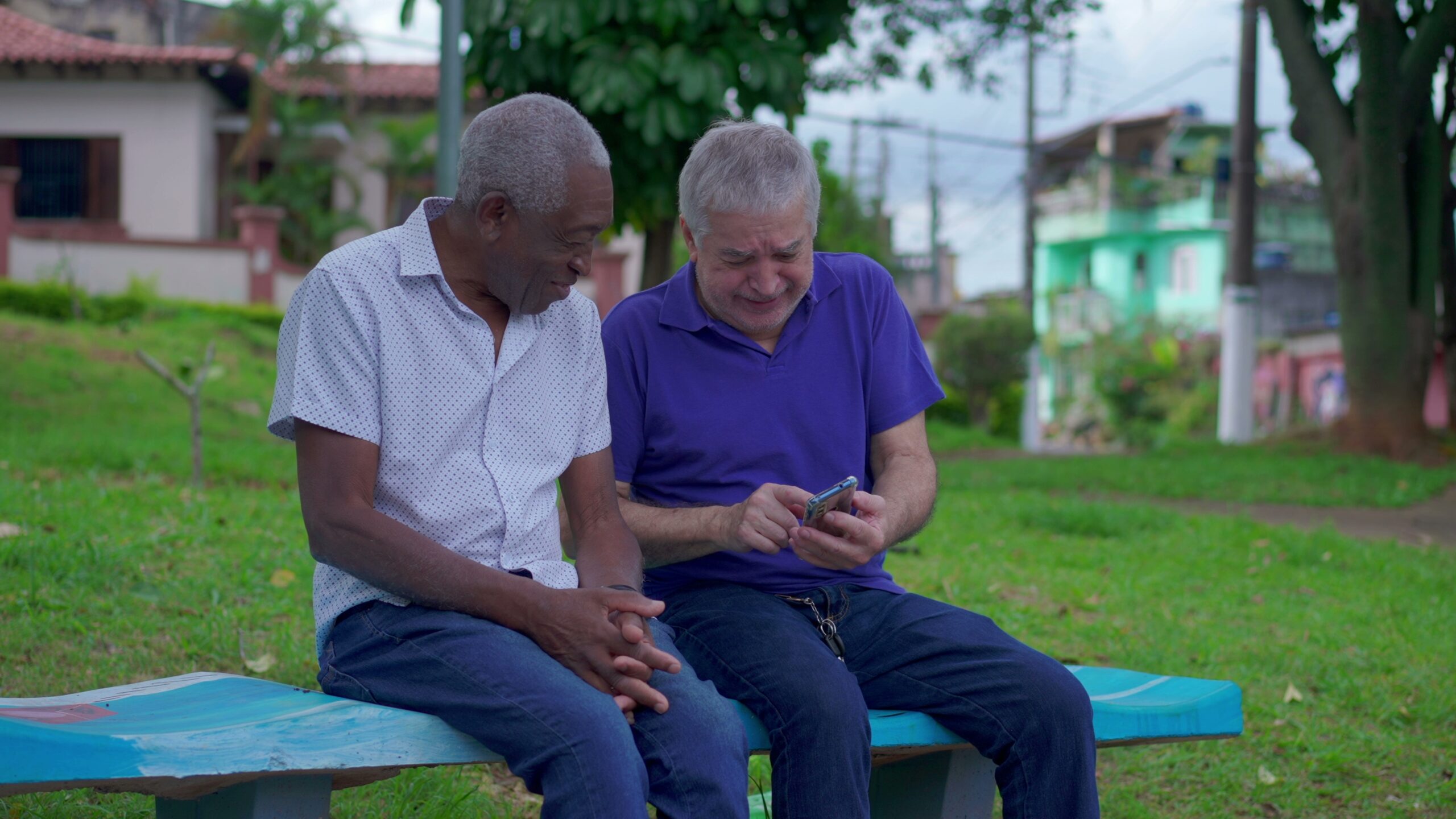Two,Diverse,Seniors,Looking,At,Phone,Sitting,On,Park,Bench